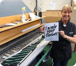 Keltic ties worker holding an ‘i made your clothes’ sign beside striped fabric, one of the uk’s trusted ties manufacturers